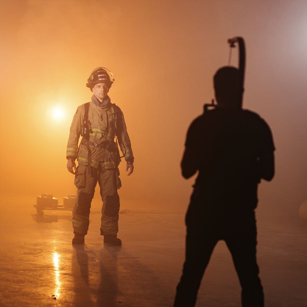 Video team filming firefighter near locker in a fiery and smokey void.