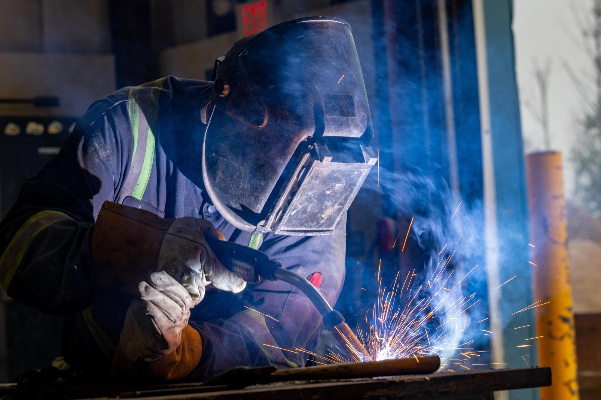 A welder using a welding torch while wearing a welding mask.